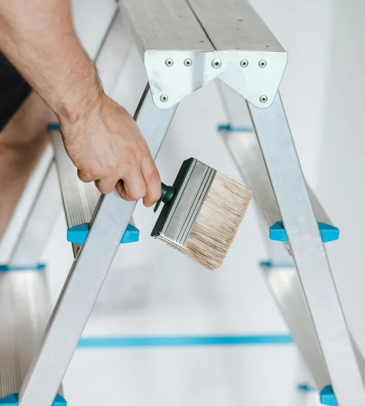 Close-up of a painter on a ladder holding a wide