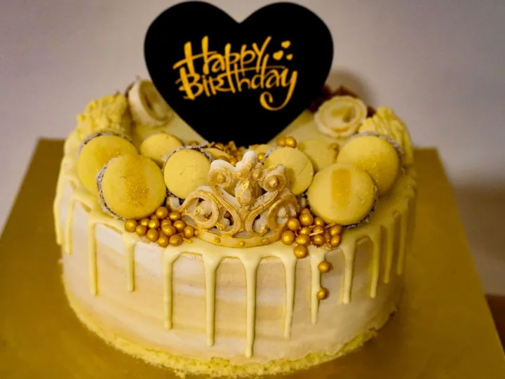 Stylish yellow birthday cake adorned with macarons and golde