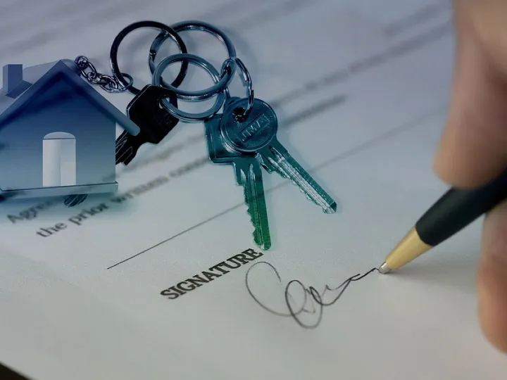 Hand signing a property contract beside a set of house keys