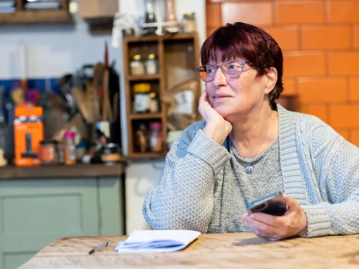 A woman sitting at a kitchen table holding a mobile phone and considering what to make of it