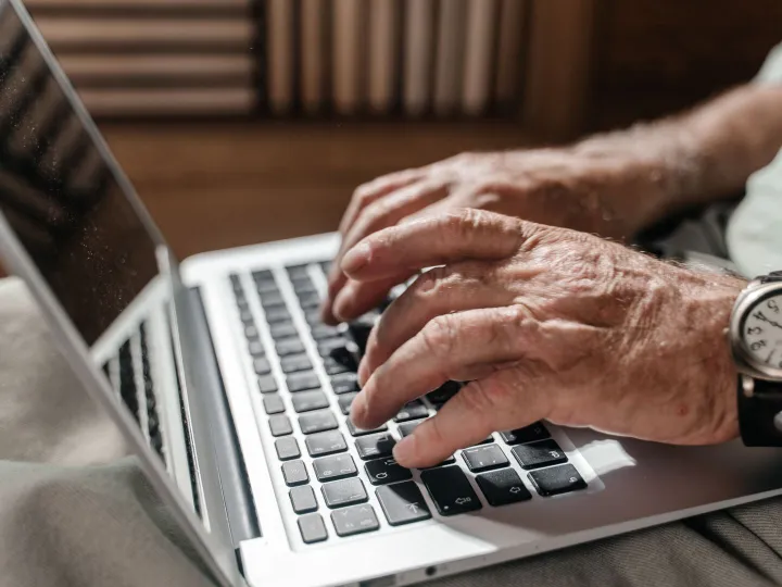 The hands of an older person typing on a laptop keyboard