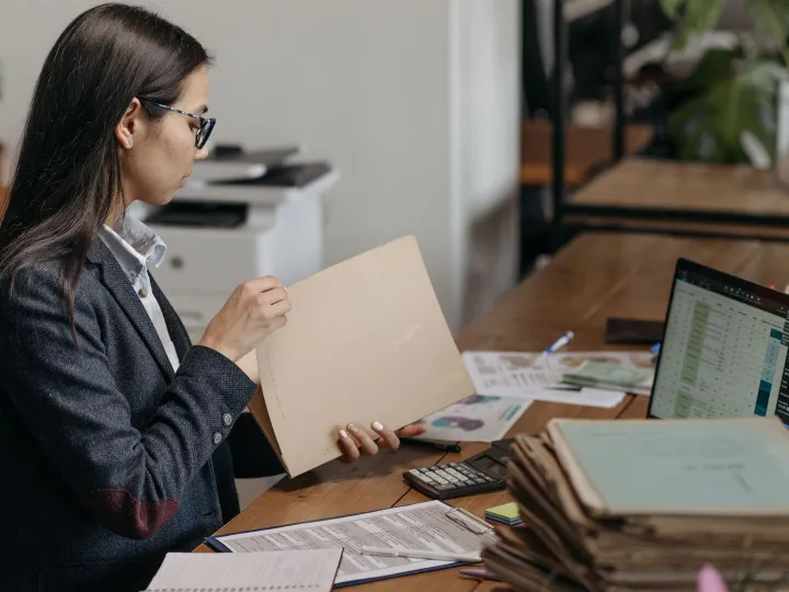 Nursery owner reading a document folder at a desk with paperwork and a laptop
