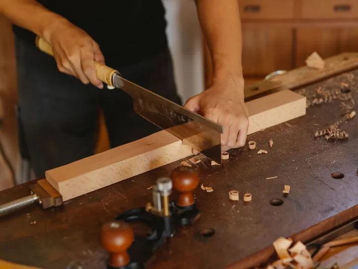 Carpenter cutting a length of timber with a hand saw at a workbench