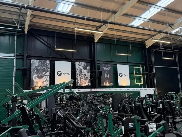 Gym hall with dark green and black painted walls, exposed roof trusses and rows of strength machines