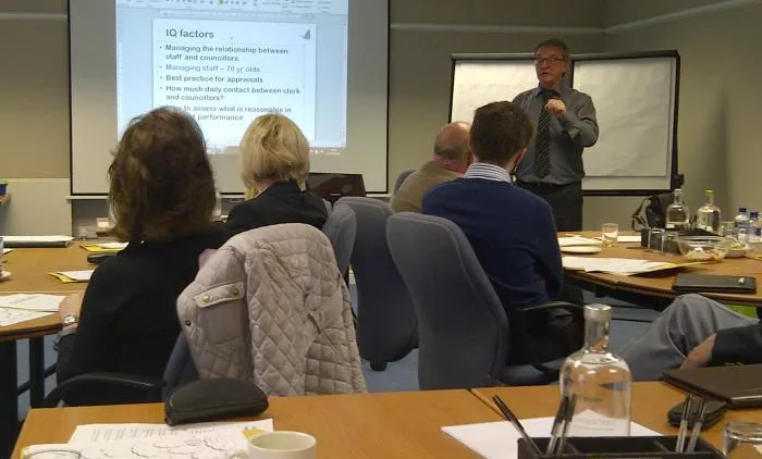 A trainer presenting a slide to delegates seated at tables during a training session