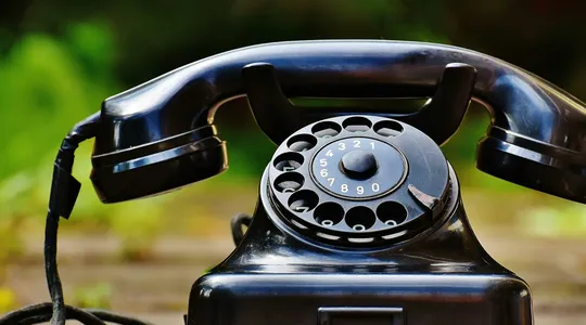 Close-up of a classic black rotary phone outdoors with a blurred green background.