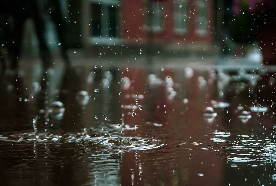Close-up of raindrops splashing into a puddle, capturing reflections and textures in an outdoor urban setting.