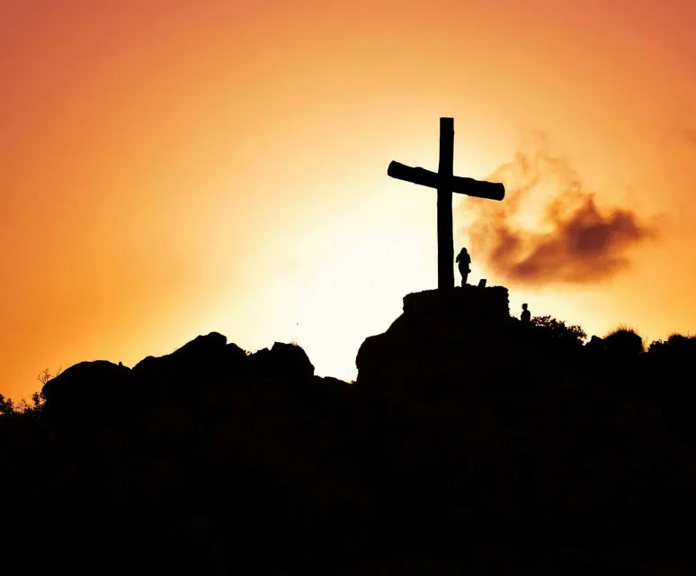 Majestic silhouette of a cross on a hill during a vivid sunset, symbolizing spirituality.