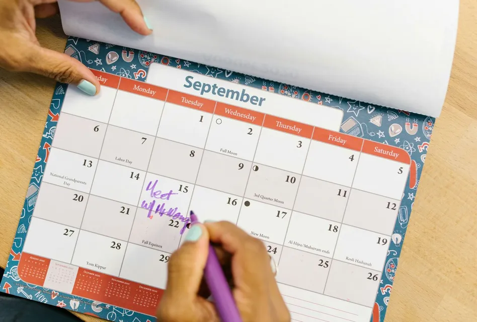 A person marking a calendar in September with a purple pen on a wooden desk.