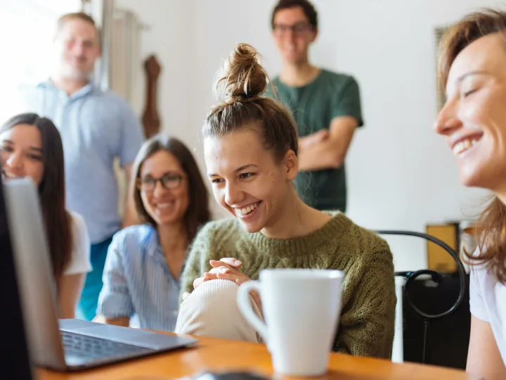 A group of friends enjoying a moment together indoors, smiling and watching a video on a laptop.