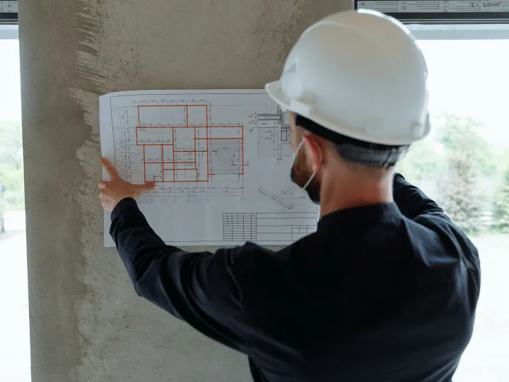 Engineer in hardhat reviewing architectural floor plans at construction site.