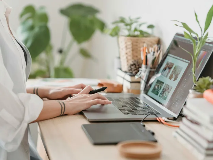 Freelance designer working from home using a laptop and digital tablet, surrounded by plants.