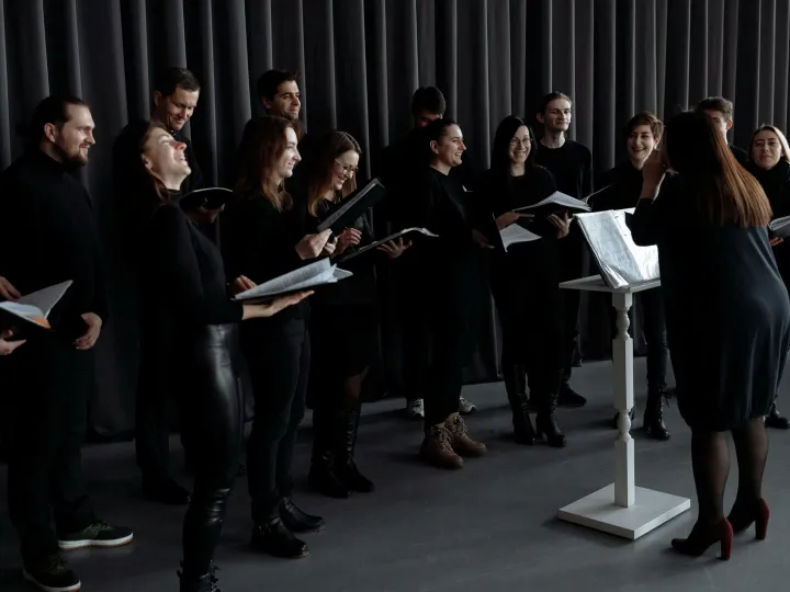A group of men and women singing with a conductor during choir practice.