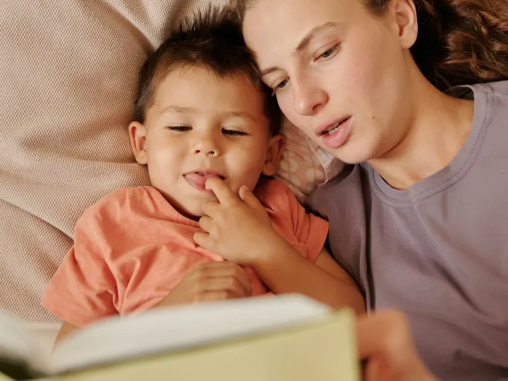 A loving mother and her young son enjoy reading a book together in bed. Captured in a cozy home setting.