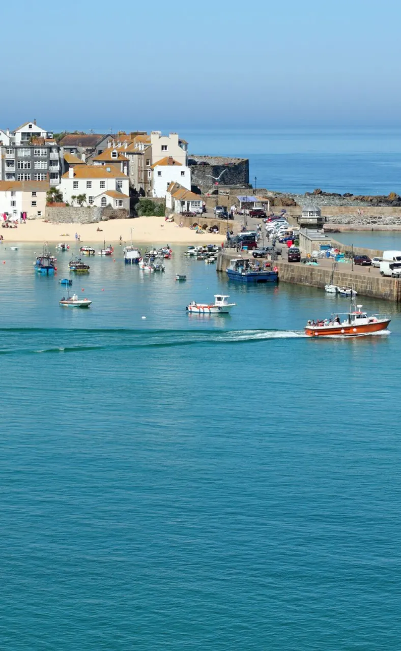 A Cornish harbour with fishing boats, a lighthouse and a sandy beach