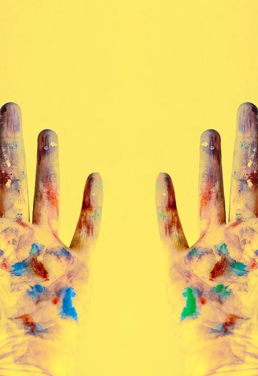 A child's paint-covered hands raised against a yellow background