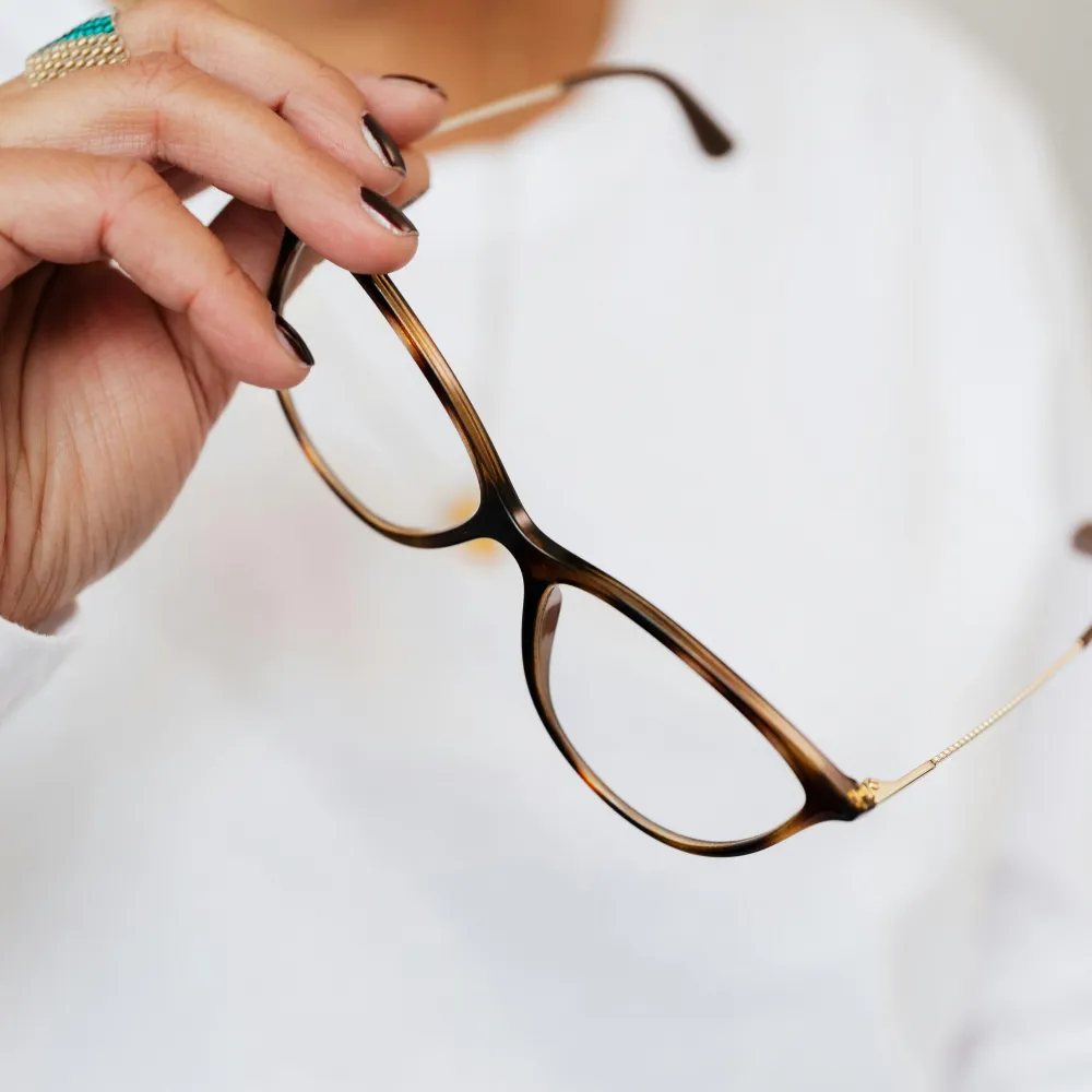 Crop unrecognizable elegant woman in white sweater and trendy optical glasses with brown frames and golden temples in hand