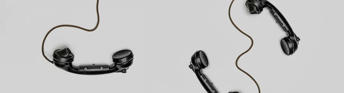 Two vintage black telephone handsets connected by cords on gray background.