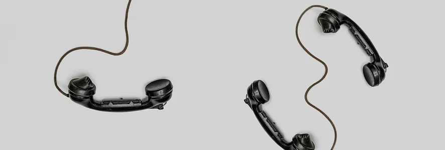 Two vintage black telephone handsets connected by cords on gray background.