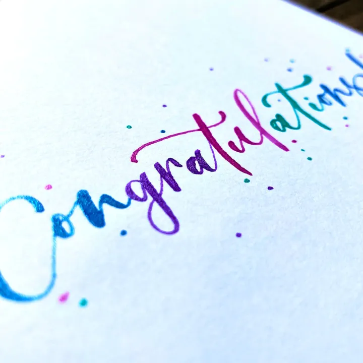 Congratulations in rainbow watercolour brush lettering on white card