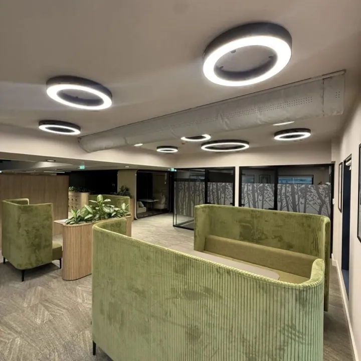Open breakout space with green velvet booths, a fluted planter, ring lights and glazed meeting rooms