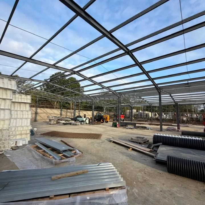 Dark painted steel portal frame with stacked roof sheets and drainage pipe on the site slab
