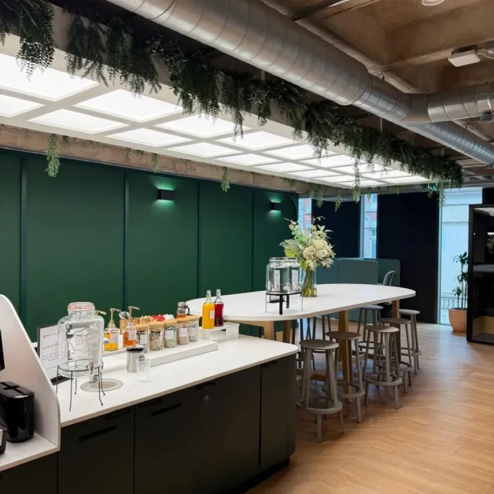 Office tea point with deep green panelled walls, a white worktop drinks station and a high table with stools