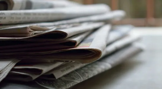 A close-up of a stack of newspapers resting on a desk, symbolizing information and media.