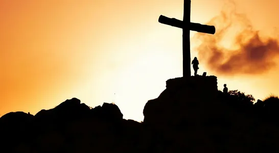 Majestic silhouette of a cross on a hill during a vivid sunset, symbolizing spirituality.