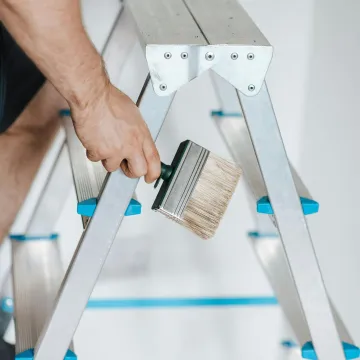 Close-up of a painter on a ladder holding a wide