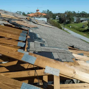 Damaged house roof with missing shingles after hurricane Ian