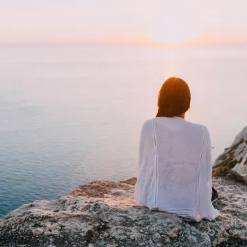 Woman Sitting on Gray Rock Near Body of Water