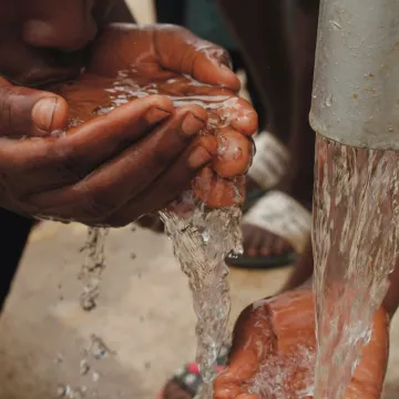 Close-up of hands and face drinking fresh water from an outdoor tap, emphasizing refreshment and necessity.