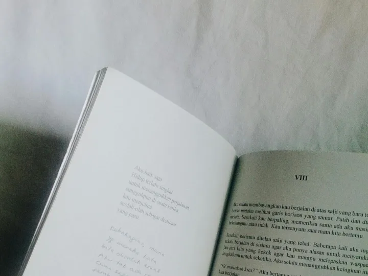 Open book with text on white surface, minimalist and monochrome style.