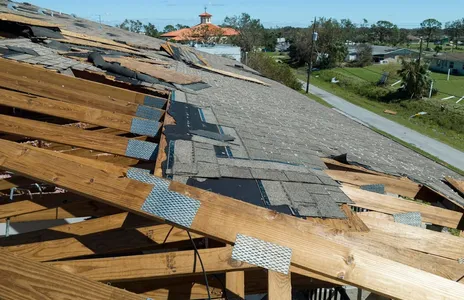 Damaged house roof with missing shingles after hurricane Ian