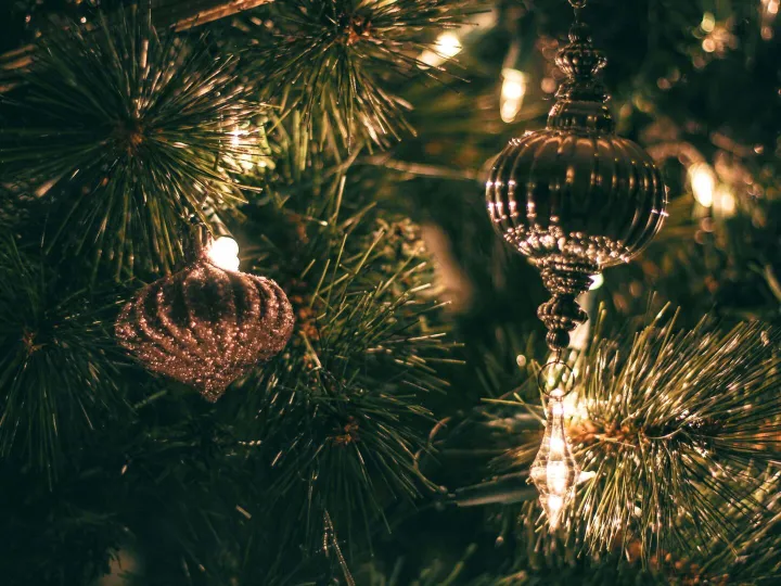 Close-up of sparkling Christmas ornaments hanging on a decorated tree with warm lights.