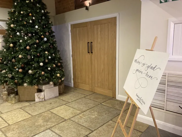 Hand lettered wedding welcome sign on an easel beside a Christmas tree