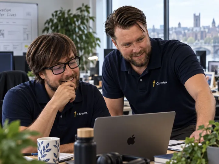 John and Toby from the Chrestos team, in Chrestos polo shirts, smiling at a laptop