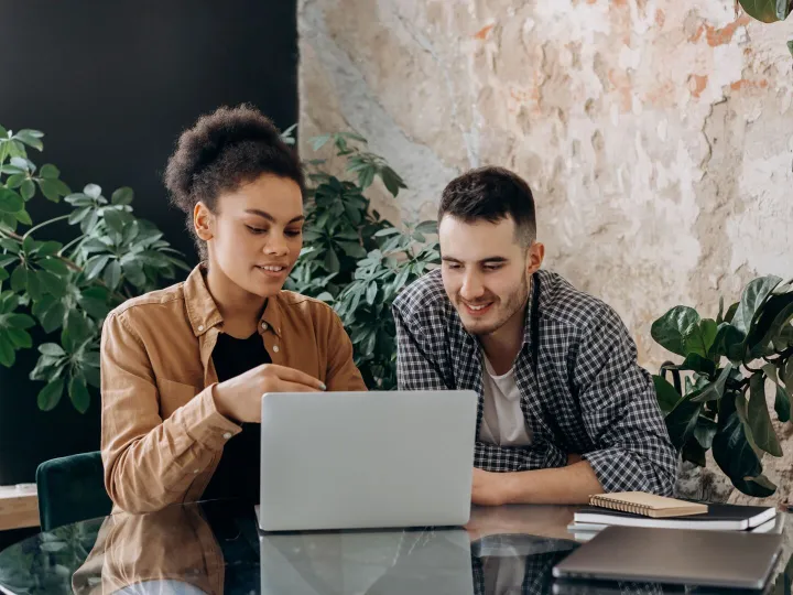Two colleagues sitting together looking at the same laptop screen