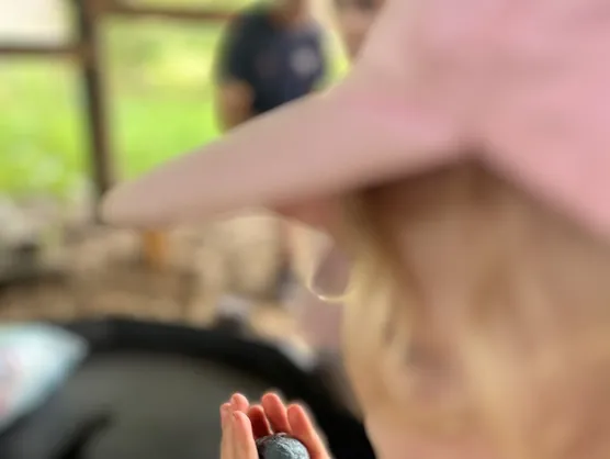 A child in a pink sun hat holding a small ball of clay in both hands
