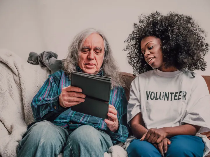 Young volunteer helping an older man use a tablet