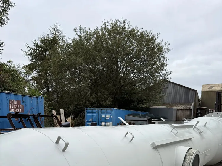 Primed light grey steel chimney section with lifting lugs and a round side port, laid out on a gravel yard