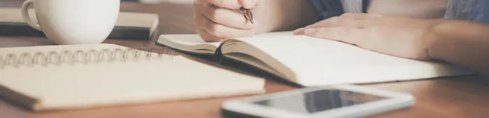 Woman Writing on a Notebook Beside Teacup and Tablet Computer