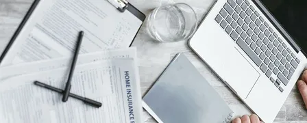 Person Writing on White Paper Beside Clear Glass Mug and Silver Macbook