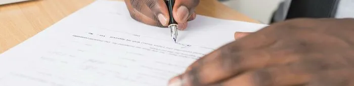 Person Holding Gray Twist Pen and White Printer Paper on Brown Wooden Table