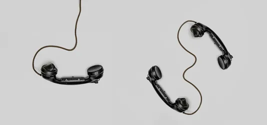 Two vintage black telephone handsets connected by cords on gray background.