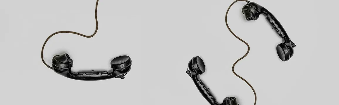 Two vintage black telephone handsets connected by cords on gray background.