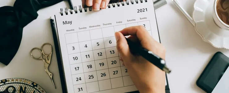 Top view of hands using a planner with coffee and accessories, focused on May 2021 calendar.