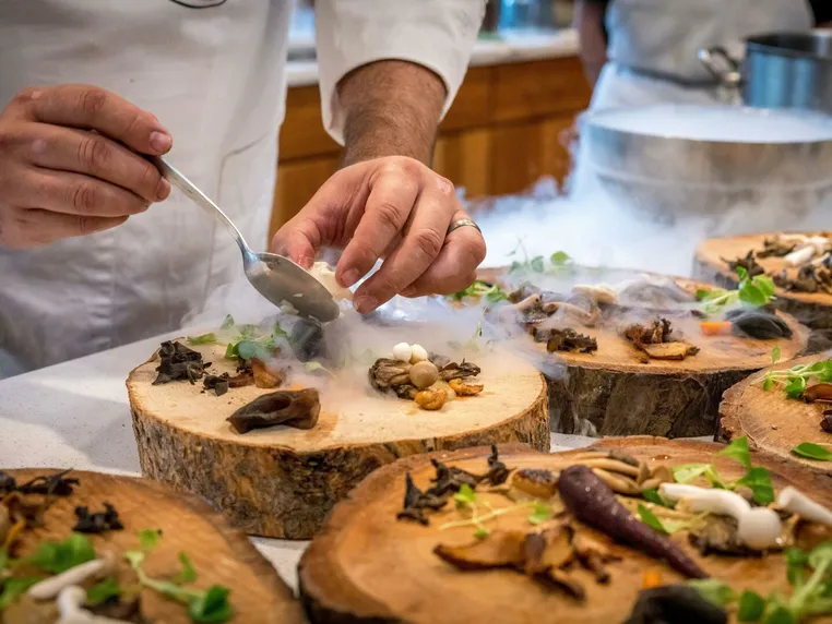 A chef plating dishes on wooden rounds, with dry-ice smoke