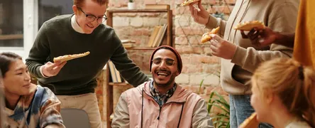 A joyful group of diverse friends enjoying pizza together in a cozy indoor setting.